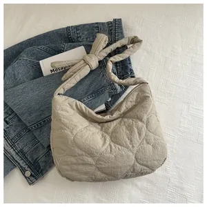 Detail of beige heart-quilted canvas shoulder bag featuring a decorative knotted shoulder strap