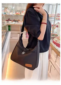 Detail of black waterproof nylon dumpling bag with silver zipper and leather patch accent