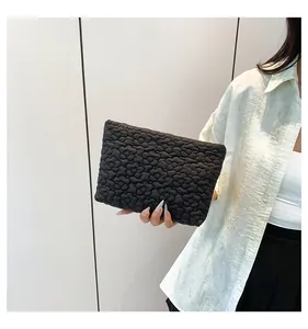 Close-up of black quilted clutch bag with floral puff texture held by a model