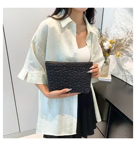 Close-up of black quilted clutch with textured 3D flower pattern and zipper closure