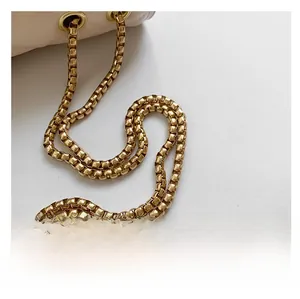 Detail of the golden box-style metal chain strap on a cream quilted leather bag
