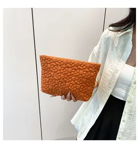 Detail of orange quilted clutch featuring embossed 3D floral texture held by a model