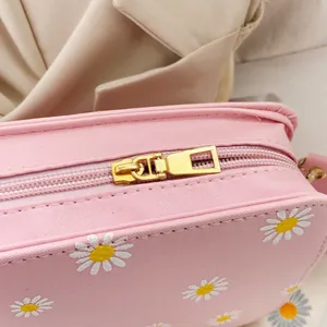 Detail of pink small crossbody bag with white daisy prints and gold zipper hardware
