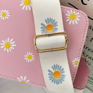 Detail of pink crossbody bag with daisy prints and wide fabric strap with golden buckle