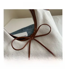 Detail view of the beige herringbone tote bag showing brown leather trim and bow knot