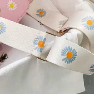Close-up of pink crossbody bag with daisy print canvas strap and gold hardware