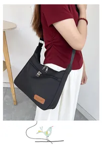 Detail of waterproof black nylon crossbody bag featuring double zip pockets and leather patch
