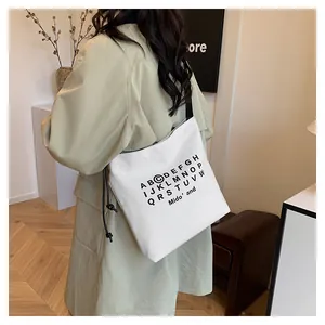 Dettaglio della borsa tote in tela bianca con stampa di lettere e tracolla sottile a coulisse
