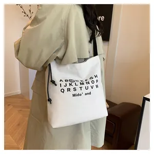 Dettaglio della borsa tote in tela bianca con stampa di lettere e coulisse nera sulla modella