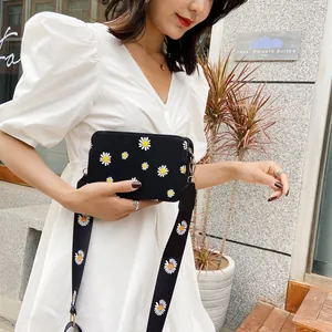 Detail of black crossbody bag with white daisy print and wide strap on model