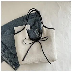 Detail of white canvas tote bag with black oversized bow and contrast leather trim