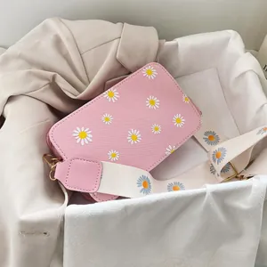 Close-up of pink crossbody bag with white daisy prints and a wide floral fabric strap