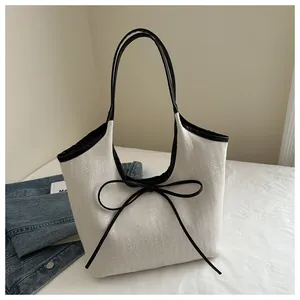 Detail of herringbone weave tote bag featuring black contrast trim and a delicate bow tie