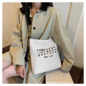 Dettaglio di una borsa tote in tela beige con stampa di lettere nere e tracolla regolabile