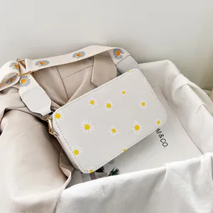 Detailed macro view of white daisy print on canvas crossbody bag with gold metal hardware