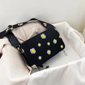 Detail of black canvas bag with daisy print, gold metal buckle and wide textile strap