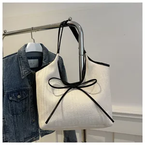 Detail of white tote bag featuring woven texture and a decorative black bow accent