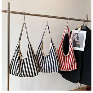 Trois sacs cabas en toile rayée en noir, bleu et rouge suspendus à des cintres inox
