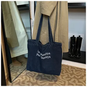 Detail of blue denim tote bag with Less Mondays More Sundays white embroidery text