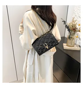 Detail of a black quilted crossbody bag featuring a golden chain strap and lock clasp