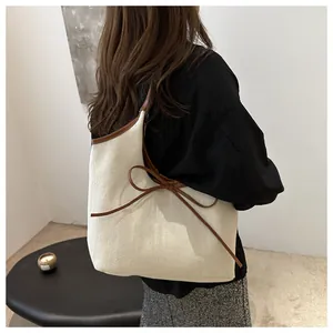 Detail of off-white canvas tote bag with brown leather bow and trim shown on model
