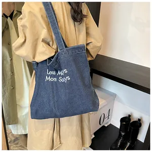 Close-up of a blue denim tote bag with white embroidery featuring a vintage shoulder strap