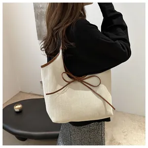 Detail of herringbone tote bag with brown leather handles and a delicate bow accent
