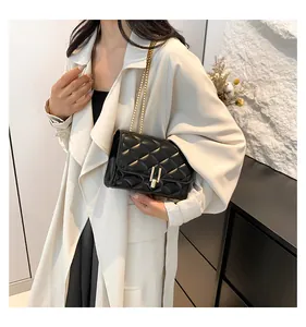 Detail of black quilted leather shoulder bag with gold chain strap on a trench coat