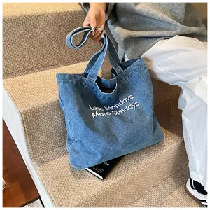 Detail of blue denim tote bag featuring embroidered text and spacious canvas design