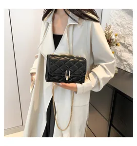 Close-up of black quilted shoulder bag with gold chain strap worn on a beige trench coat