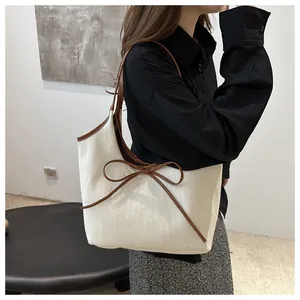 Detail shot of the cream canvas tote bag featuring a decorative brown leather bow