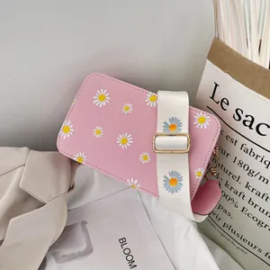 Detailed shot of pink crossbody bag with daisy prints and a wide fabric strap with blue flowers