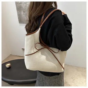 Detailed view of cream woven tote bag with brown leather trim and bow on a model