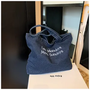 Detail of dark blue denim tote bag featuring white Less Mondays More Sundays embroidery