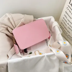 Detail of pink faux leather crossbody bag with daisy pattern wide fabric strap and gold hardware