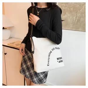 Vista laterale di una borsa tote in tela bianca con spalline nere e dettaglio nodo sulla spalla