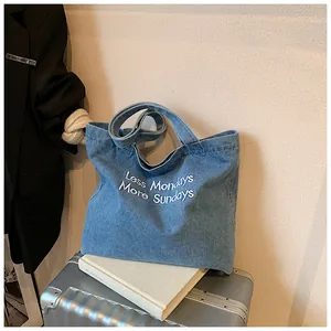 Detail of blue denim tote bag with Less Mondays More Sundays embroidery on silver suitcase