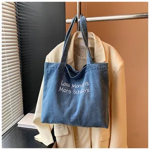 Detailed close-up of blue denim tote bag with white Less Mondays More Sundays embroidery