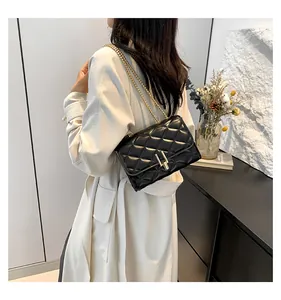 Detail of a black quilted chain bag with gold lock worn over a beige trench coat