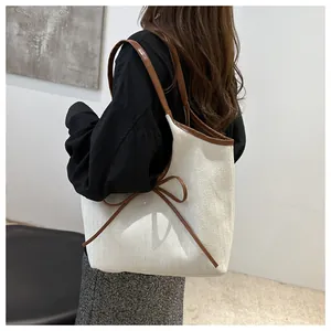 Detail of herringbone canvas tote bag showing the side leather bow and premium texture