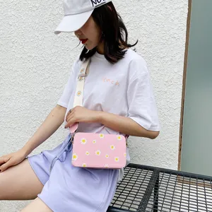 Detailed outdoor shot of a pink crossbody bag featuring daisy prints and a wide strap