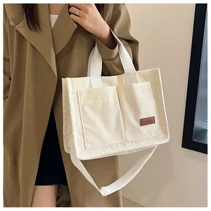 Close-up of cream corduroy tote bag showing dual front pockets and fashion leather label