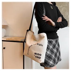 Dettaglio della borsa tote in tela bianco avorio con scritte artistiche e tracolla nera annodata