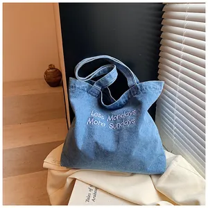 Detail of light blue washed denim tote bag with white Less Mondays More Sundays embroidery