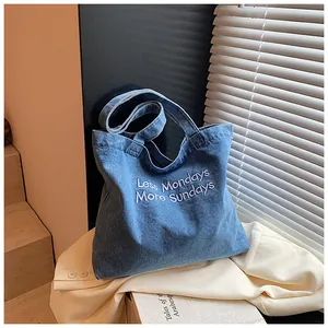 Macro detail of blue washed denim tote bag featuring white embroidered text and wide handles