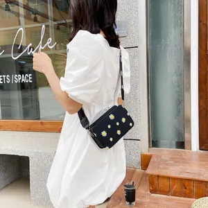 Black crossbody square bag with daisy print and wide strap on white dress model