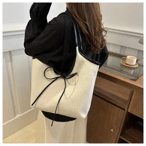 Detail of cream woven tote bag featuring black leather trim and decorative bow accent