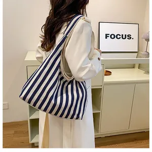 Sac hobo en toile rayé bleu marine et beige porté par un mannequin en décor épuré