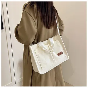 Detail of a large corduroy tote bag in off-white with double front pockets and brown label