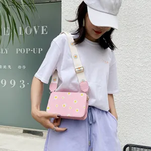Pink daisy print crossbody bag with wide shoulder strap in outdoor fashion scene